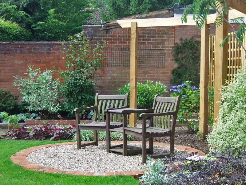 Traditional garden with small gravel seating area framed by an arbour rail