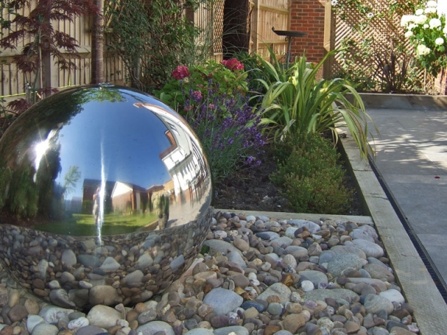 Stainless steel sphere recycling water feature reflects the surrounding garden