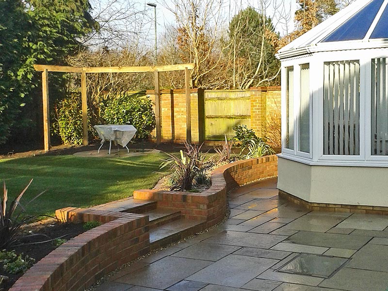 The lower patio leads up to a raised level lawn with stone circle paving framed by an arbout rail