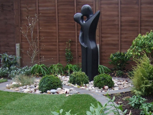 Contemporary statue set in a circular bed with pebbles and Box Balls