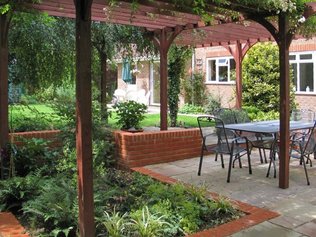 Shady sunken patio with brick edging framed by a pergola
