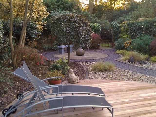 Enclosed garden with decking, slate paths and a circular patio and spherical water feature
