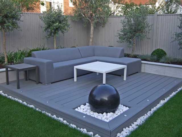 Contemporary outdoor lounge with composite decking and spherical granite water feature in constrained palette of greens and grey