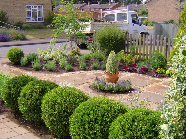 Curving design with stepping stones and gravel. A central pot adds height and a row of box balls screens of the driveway.