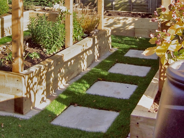 Stepping stone path through grass between sleeper raised beds